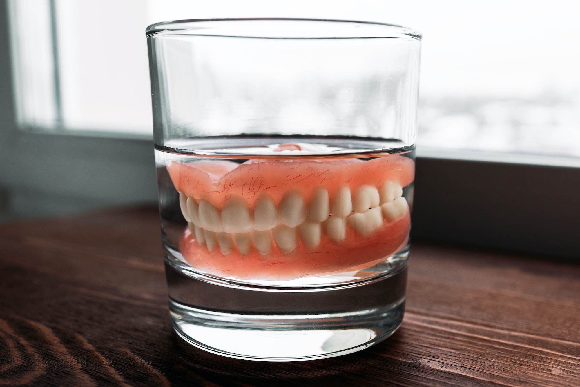 A denture in a glass of water. Dental prosthesis care. Full removable plastic denture of the jaws