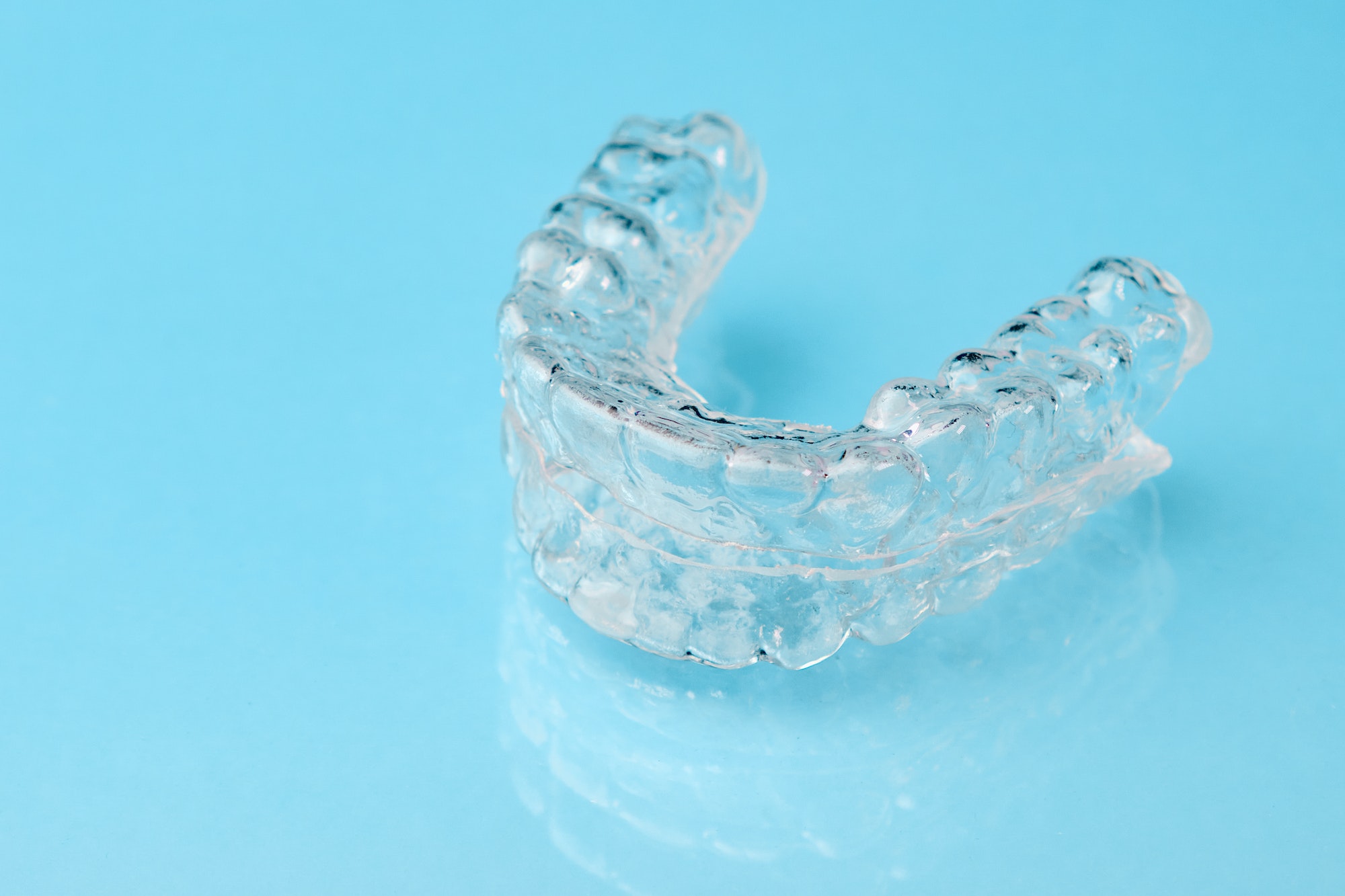 Close up invisible aligners on the blue background with copy space. Plastic braces dentistry