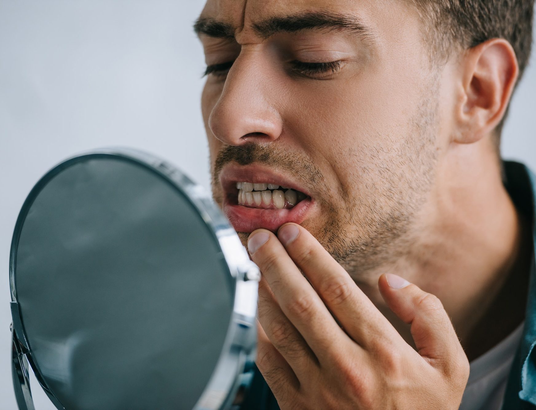 close-up view of young man with tooth pain looking at mirror